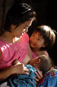 Woman nursing a baby as an older child looks on