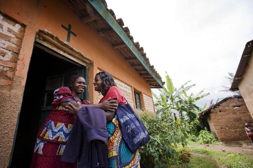 A community health worker greets a pregnant woman outsider her home in Rwanda.
