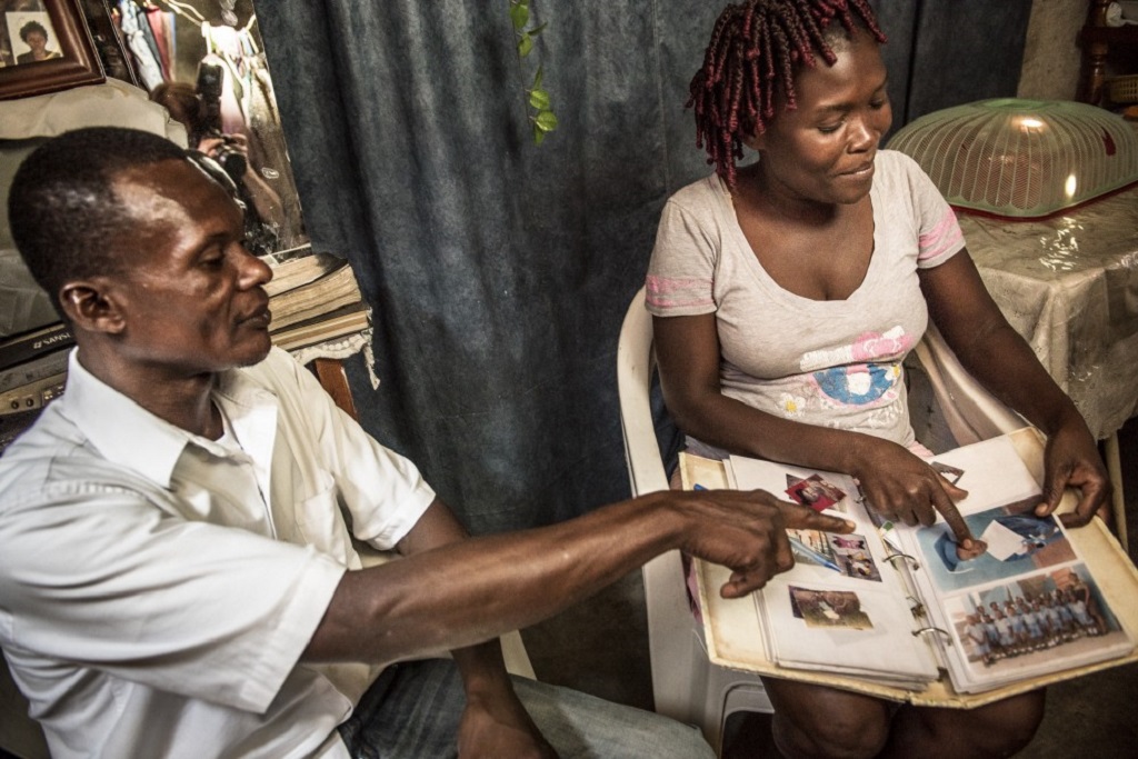 Client Dulenne Geantilhommes shows Pierre Tenor photos of her three children who are in school. Tenor helps ensure that she stays on her antiretroviral medications.