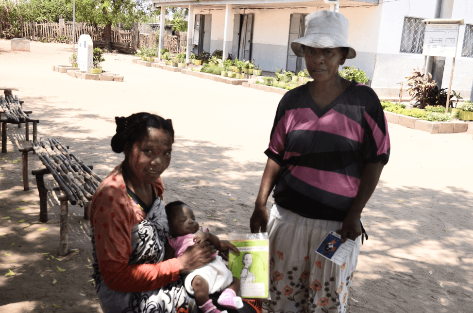 Bemanonga Health Center, Morondava, Madagascar. In her arms, Dorothée holds her daughter and the TMT card that is loaded with helpful information for young mom and first parents. Standing next to her is Roselle, a community health worker empowered by the MCSP TMT initiate. 