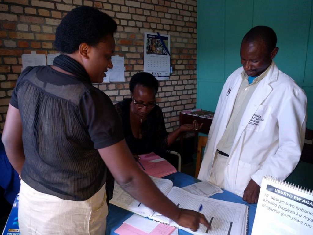 MCSP staff and a PPFP national trainer provide guidance on how to enter data in a register and client file in Kigeme, Rwanda.