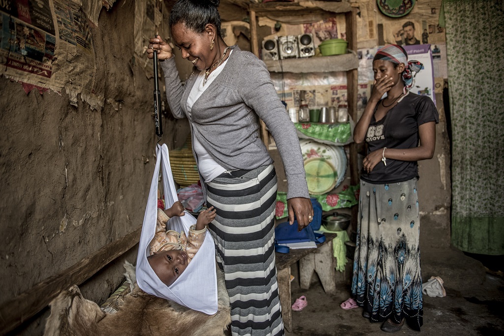 Asmamaw weighs Saleamelak while visiting the toddler and his mother, Yaregale, at home.