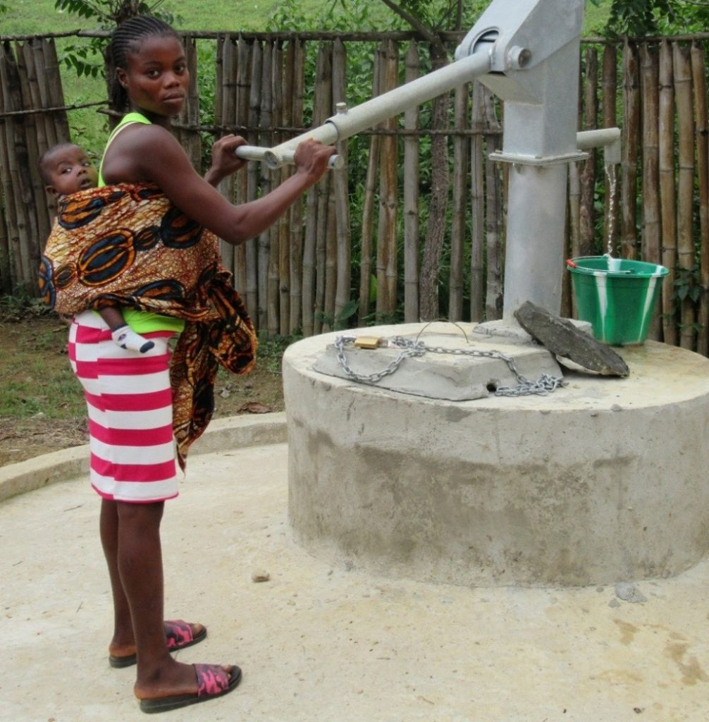 Princess Charlie, a patient at Lloydsville Clinic in Grand Bassa County, with her baby on her back at a new hand pump